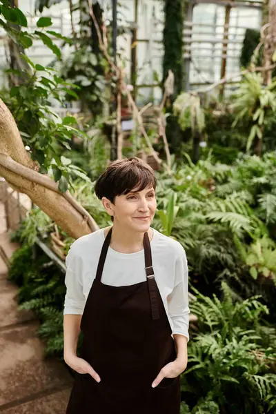 Mujer segura con cabello corto que atiende expertamente a las plantas en un floreciente entorno de invernadero - foto de stock