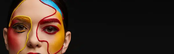 A young woman displays vibrant face art with bold designs on a dark background. — Stock Photo