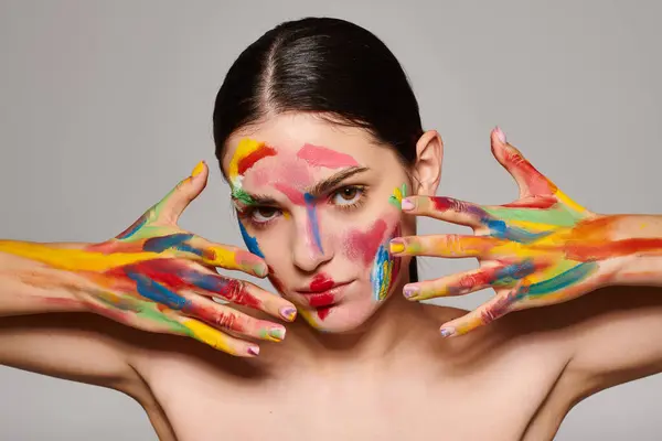 A young woman displays her creativity with vibrant face art and colorful hand makeup. — Stock Photo
