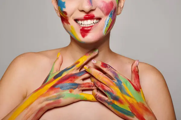 A young beautiful woman smiles radiantly, her face and hands adorned with vibrant paint. — Stock Photo