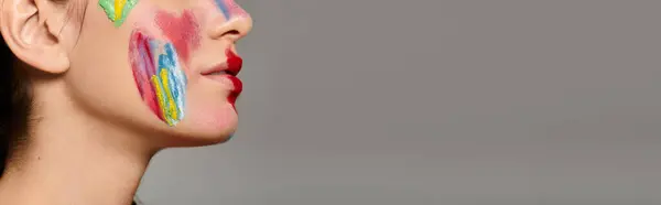 A young woman showcases vibrant face art painted on her skin and lips. — Stock Photo