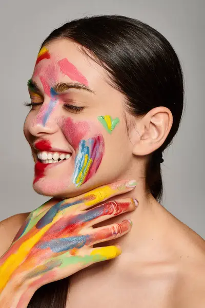 Eine schöne junge Frau lächelt strahlend, als bunte Gesichtsbemalung und Farbe ihre Gesichtszüge hervorheben. — Stockfoto