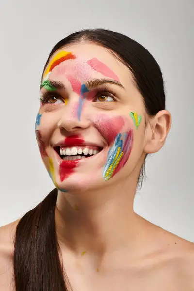 Joyful woman smiles brightly, flaunting colorful face art and vibrant makeup artistry. — Stock Photo