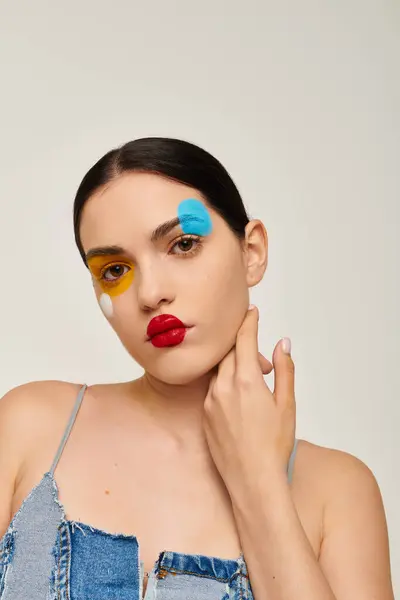 A young woman showcases vibrant face art with colorful designs highlighting her features. — Stock Photo