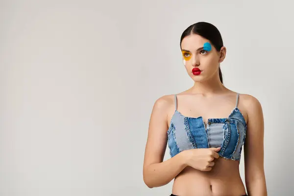 A young woman shows off artistic face paint while confidently posing in a denim top. — Stock Photo