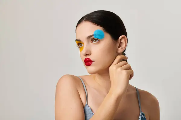 A stunning young woman displays vibrant, artistic face makeup, radiating style and creativity. — Stock Photo