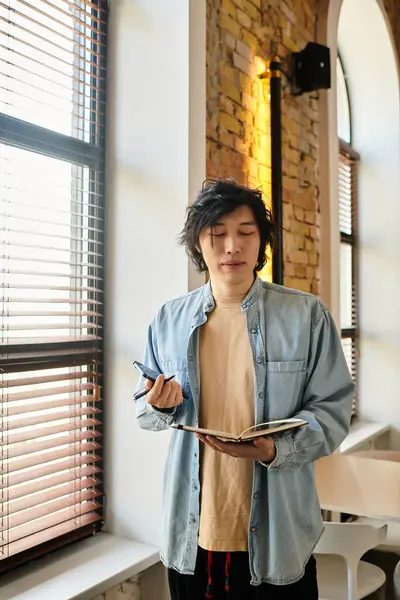A young professional stands in a bright office, pondering ideas while holding a notebook and pen. — Stock Photo