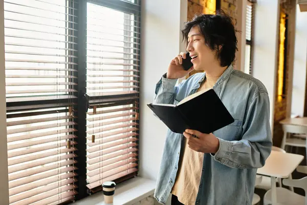 A person talks on the phone in a bright office, holding a notebook and enjoying sunlight. — Stock Photo