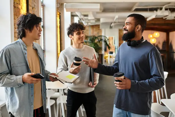 Three coworkers interact enthusiastically while enjoying coffee in a vibrant workplace. — Stock Photo