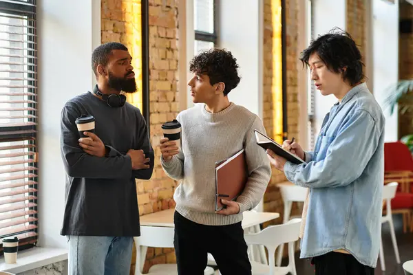 In uno spazio di lavoro luminoso, tre colleghi condividono il caffè e si scambiano entusiasticamente idee. — Foto stock