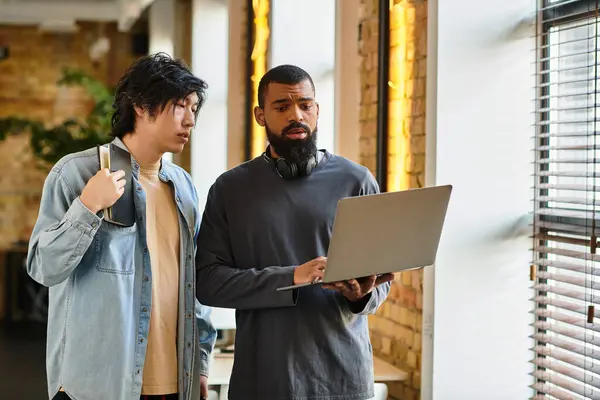 Zwei Mitarbeiter diskutieren beim Betrachten eines Laptops in einem modernen Arbeitsraum. — Stockfoto