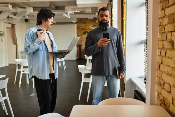 Due professionisti interagiscono in un ufficio elegante, uno utilizzando un computer portatile e l'altro su uno smartphone. — Stock Photo