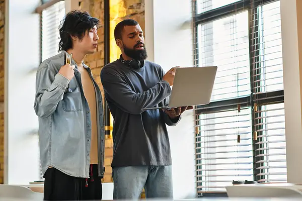 Two colleagues engage in a discussion, analyzing data on a laptop in a bright workspace. — Stock Photo