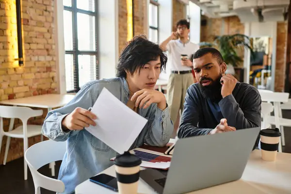 Zwei Mitarbeiter konzentrieren sich intensiv auf einen Laptop, während sie in einem kreativen Büro-Setup Ideen diskutieren. — Stockfoto
