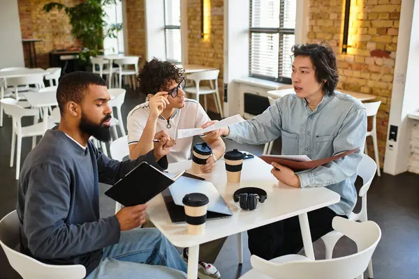 Three professionals collaborate energetically at a trendy workspace while holding coffee cups. — Stock Photo