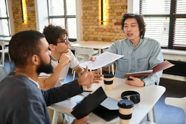 Tre professionisti si impegnano in una vivace discussione sul lavoro, condividendo idee e documenti. — Foto stock