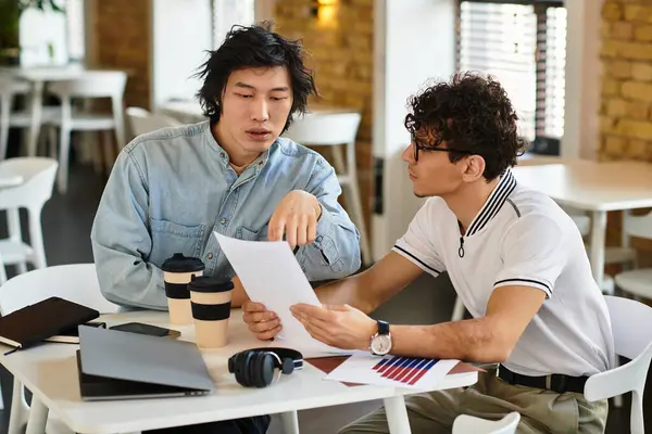 Two professionals collaborate, exchanging ideas while reviewing documents at their workspace. — Stock Photo