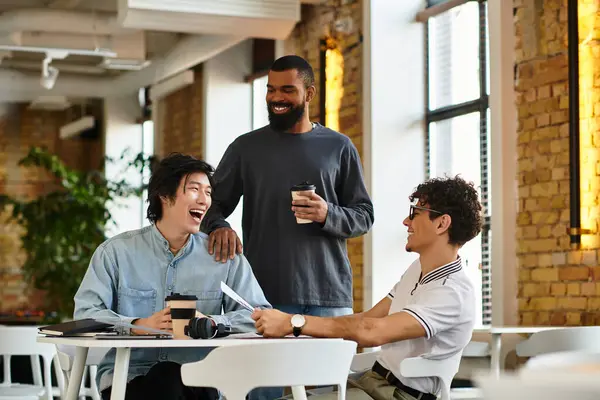 Three coworkers engage in lively conversation while enjoying coffee in a bright, modern workspace. — Stock Photo