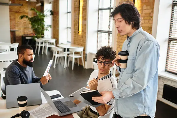 Three colleagues discuss ideas while seated in a bright, trendy office atmosphere with laptops. — Stock Photo