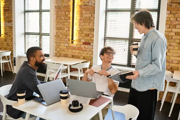 Three people chat energetically with laptops and coffee in a modern office. — Stock Photo
