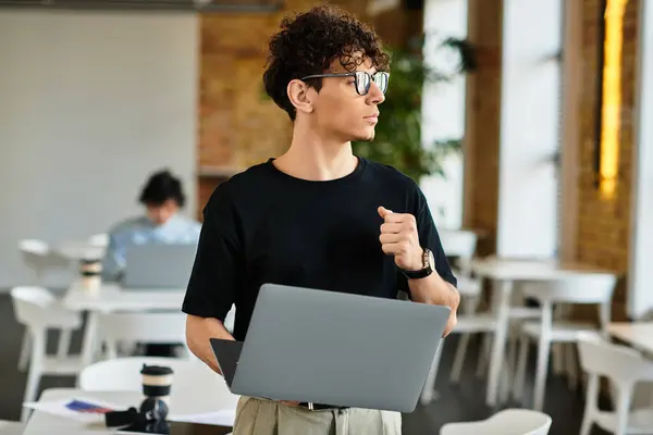 A focused individual with a laptop stands in a stylish office, brainstorming with colleagues. — Stock Photo