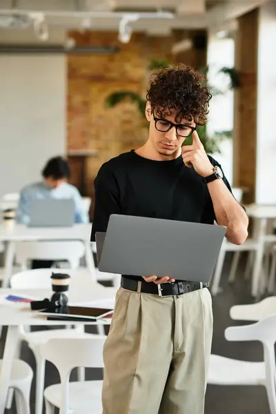 A curly haired person with glasses focuses on their laptop in a bright, stylish office. — Stock Photo