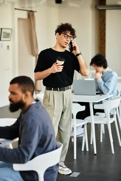 I giovani si concentrano sui compiti in uno spazio di lavoro luminoso mentre si parla al telefono con il caffè in mano — Foto stock