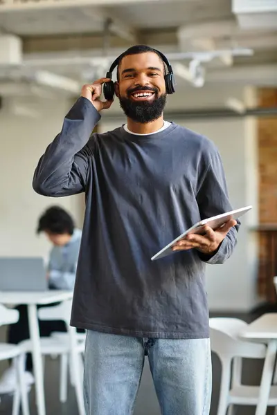 A man smiles with headphones and a tablet in a modern office during work hours. — Stock Photo