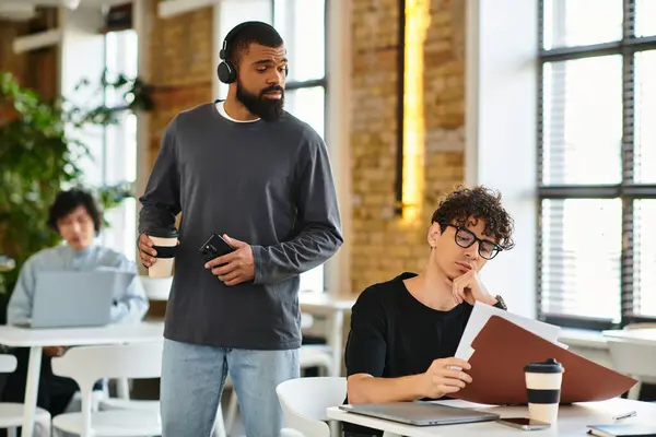 Two coworkers discuss ideas while another colleague focuses on work in a bright, inviting office. — Stock Photo
