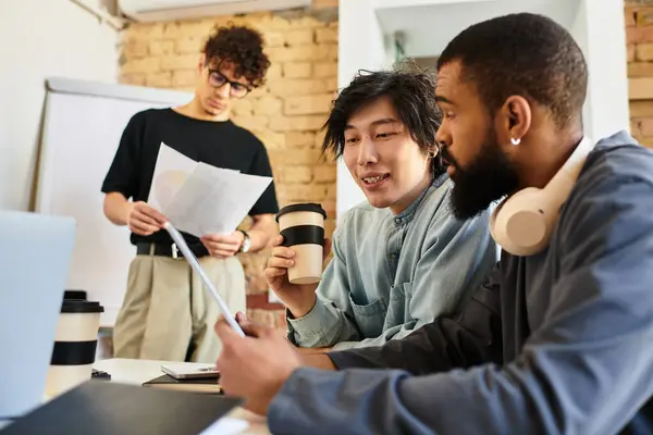 Two colleagues discuss over a laptop while a third reviews notes in a bright workspace. — Stock Photo