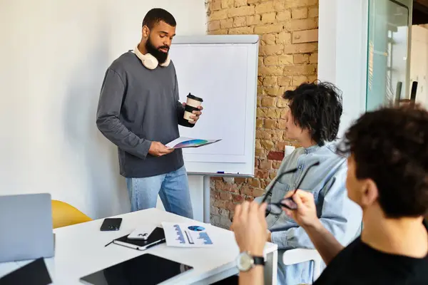 A man leads an interactive discussion at a stylish workspace, holding a clipboard and coffee. — Stock Photo