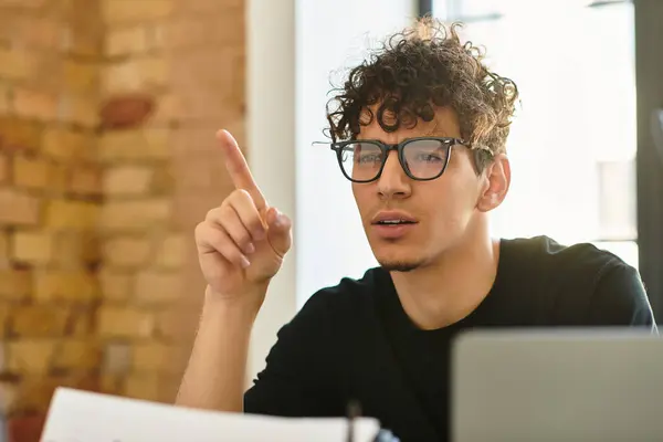 Un jeune homme concentré avec des gestes de cheveux bouclés réfléchit pendant qu'il travaille à son bureau. — Photo de stock