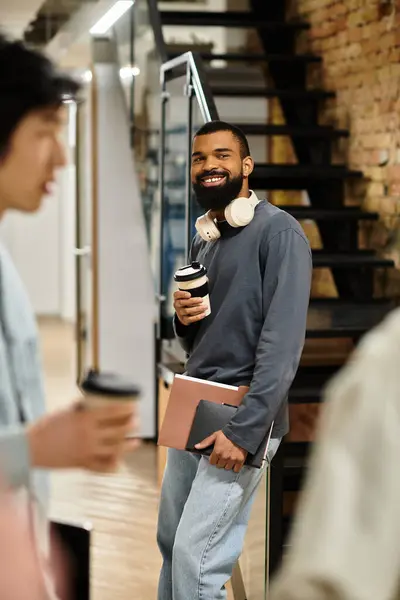 Colleagues chat casually as a man smiles and sips coffee in a lively office. — Stock Photo