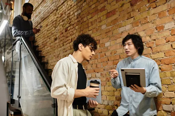 Two professionals exchange ideas while a third colleague works nearby in a creative workspace. — Stock Photo