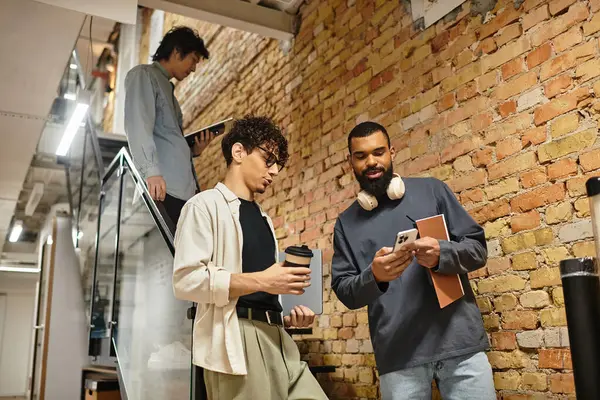 Three colleagues share ideas and coffee during a lively stairway chat in a modern workspace. — Stock Photo