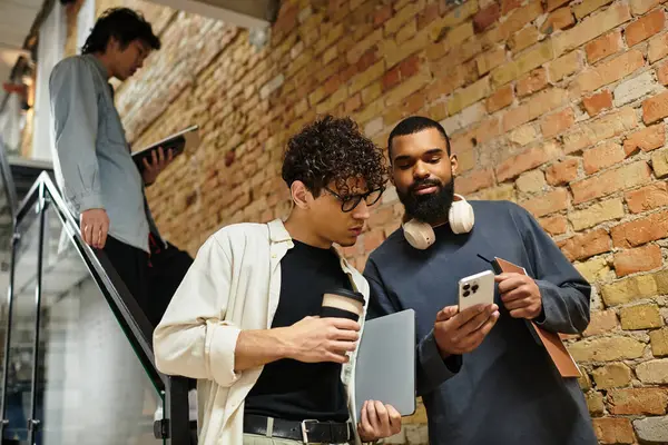 Two colleagues share ideas while reviewing a smartphone in a chic, brick walled office. — Stock Photo