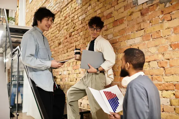 Three team members collaborate in a vibrant office, sharing ideas over coffee and tech. — Stock Photo