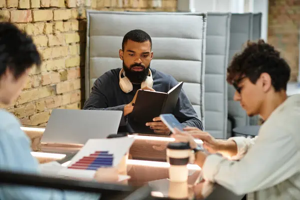 Tres personas se concentran en tareas en una oficina contemporánea, compartiendo ideas y tecnología. - foto de stock