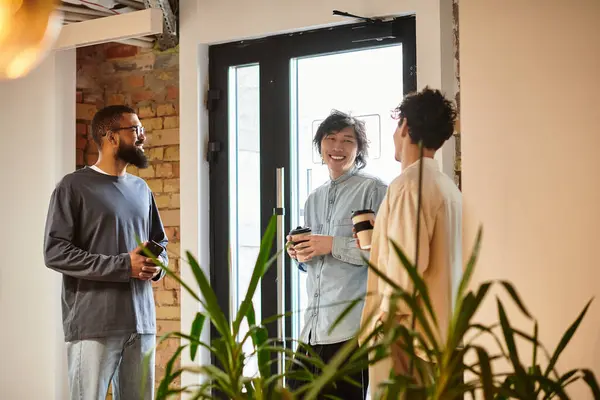Three professionals engage in friendly dialogue while enjoying coffee in a bright, airy workspace. — Stock Photo