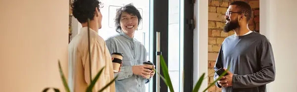 Drei Mitarbeiter diskutieren lebhaft, während sie Kaffeetassen in einem stilvollen Arbeitsbereich halten. — Stockfoto