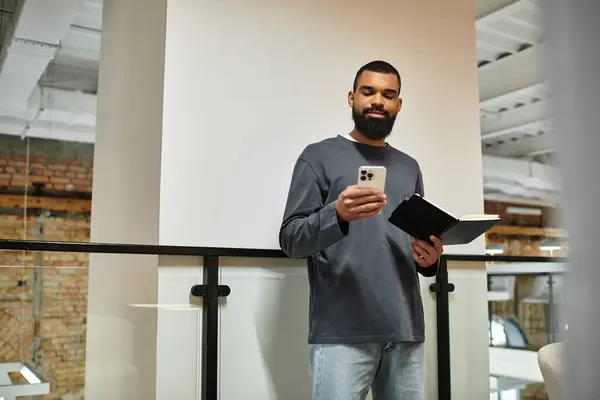 A man stands in a chic office, checking his phone and holding a notebook, exuding productivity. — Stock Photo
