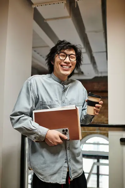 A glasses wearing man in casual attire enjoys coffee with notebooks in a vibrant workspace. — Stock Photo