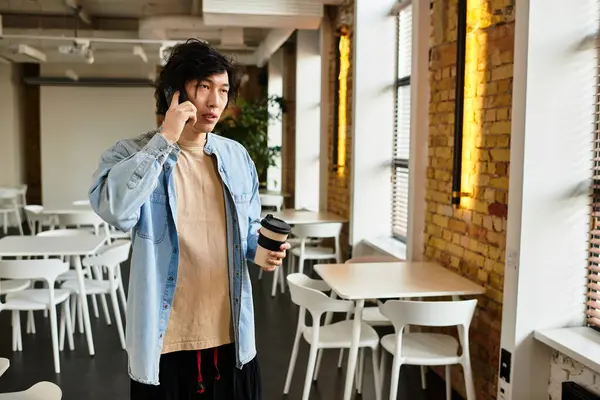 A person stands in a modern office, engaged in a phone call while holding a coffee in hand. — Stock Photo