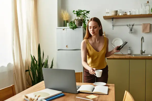 Questa giovane donna bilancia la sua routine mattutina con una tazza di caffè caldo e uno smartphone in mano. — Foto stock
