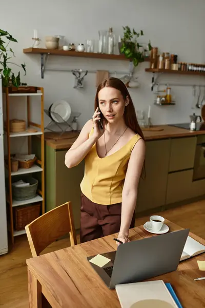 Una giovane donna in una cucina elegante parla sul suo telefono mentre fa i suoi compiti. — Foto stock