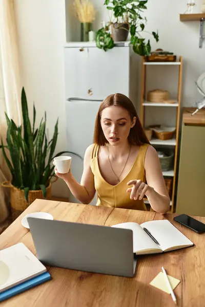 Una giovane donna gode di un caffè a un tavolo di legno, focalizzato sul suo computer portatile e immerso nel lavoro. — Foto stock