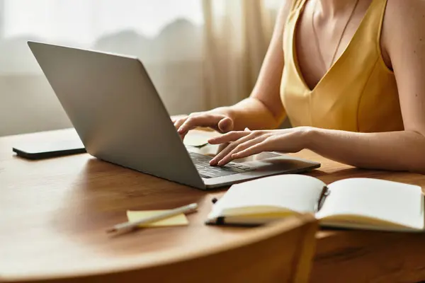 In a bright room, a young woman types intently on her laptop at a wooden table. — Stock Photo