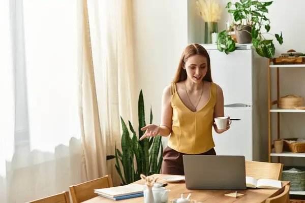 A young woman holds a coffee cup while chatting animatedly at her modern home workspace. — Stock Photo