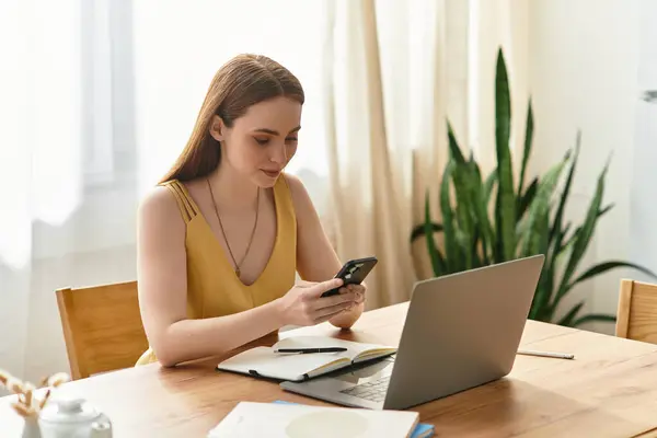 Beautiful young woman engages with her smartphone at a wooden table in a cozy home setting. — Stock Photo