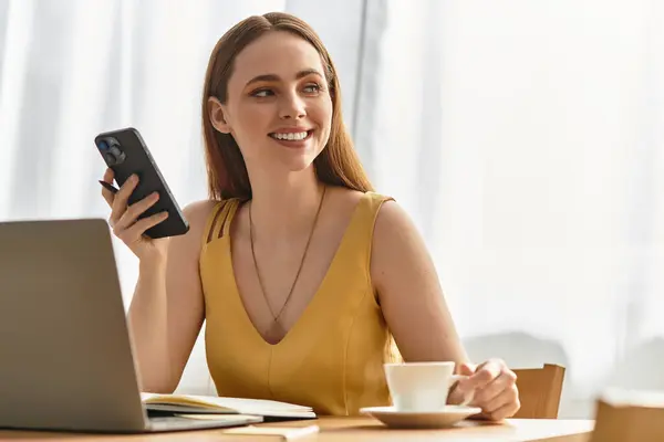 Brightly lit cafe features a young woman smiling as she holds a phone, enjoying a warm beverage. — Stock Photo